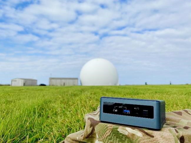 Image shows hand held radar in a field with a Radome satellite dome in the background.